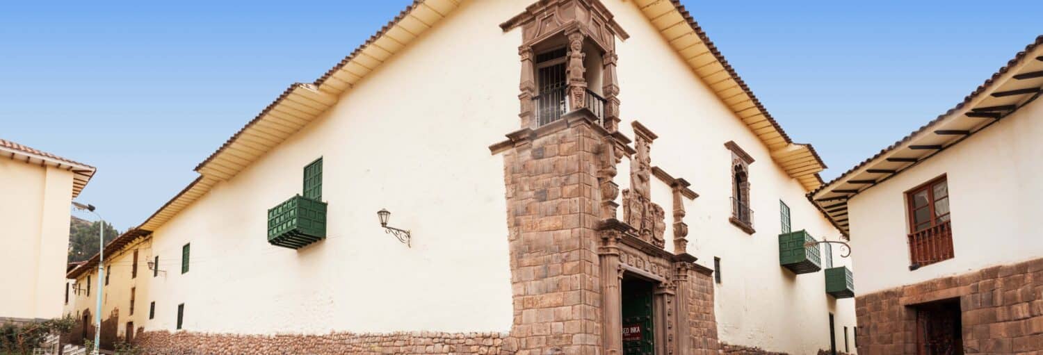 Um edifício histórico branco com uma entrada de pedra e persianas verdes, em um céu azul claro na Visita guiada por Cusco e pelo Museu Inca