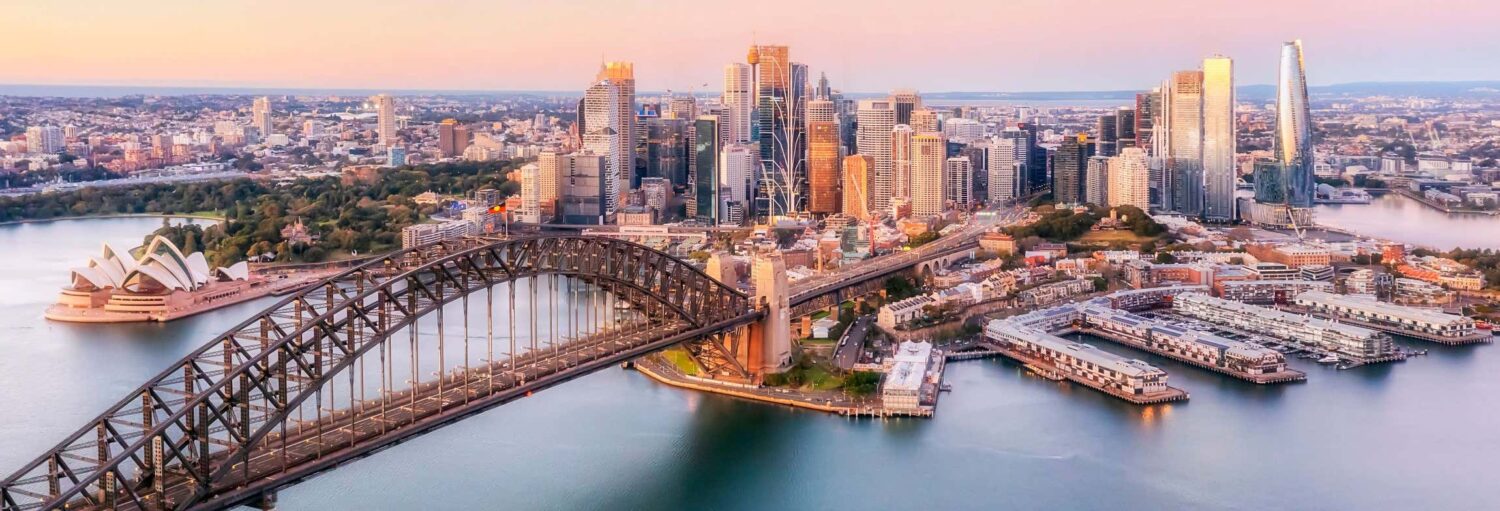 Vista aérea de Sydney com a Harbour Bridge, a Opera House e o horizonte da cidade ao nascer do sol. Imagem para ilustrar post sobre tour por Sydney.