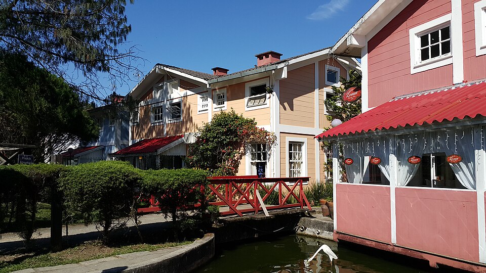 Duas casas em tons pastéis na Pequena Finlândia em Penedo com telhados vermelhos ficam ao lado de um pequeno canal e de uma ponte de madeira em um dia ensolarado.