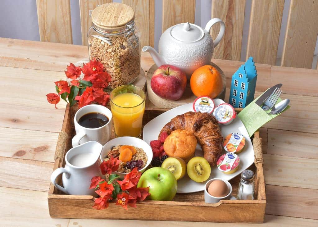Uma bandeja de café da manhã do Turquoise B&B com croissant, frutas, suco, café, chá, iogurte, cereais, um ovo cozido e um pote de granola.