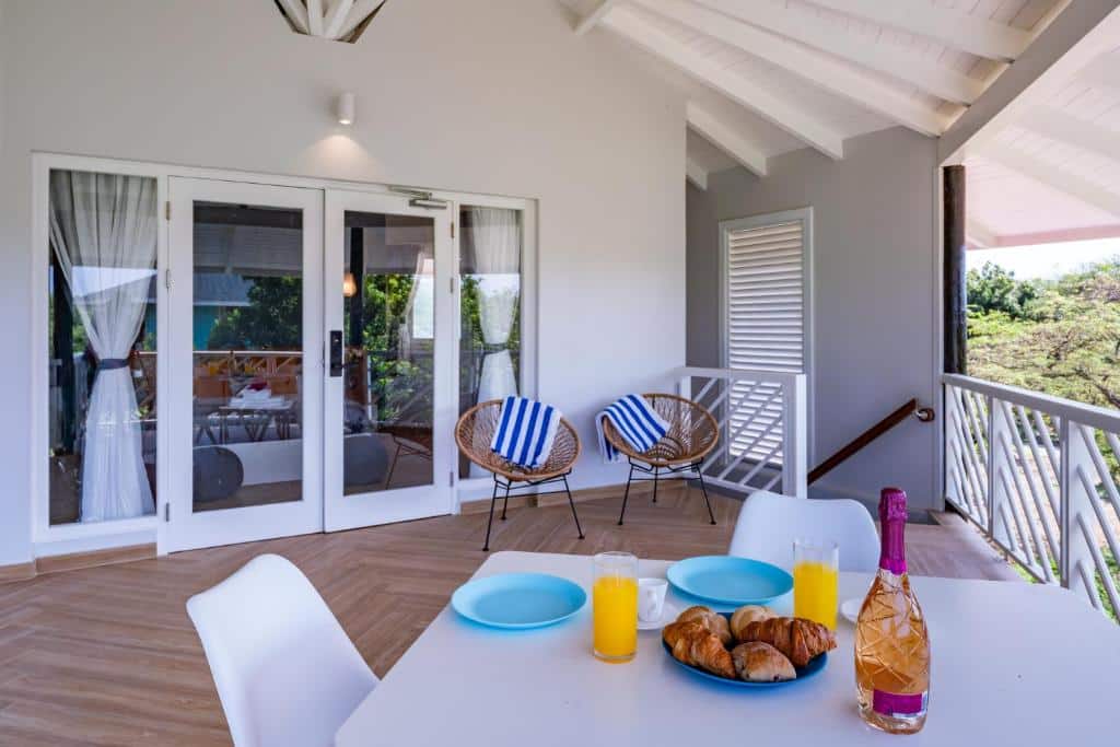 Uma mesa do Bed & Bike Westpunt com croissants, suco de laranja e uma garrafa fica em uma varanda com duas cadeiras e portas de vidro para uma casa.