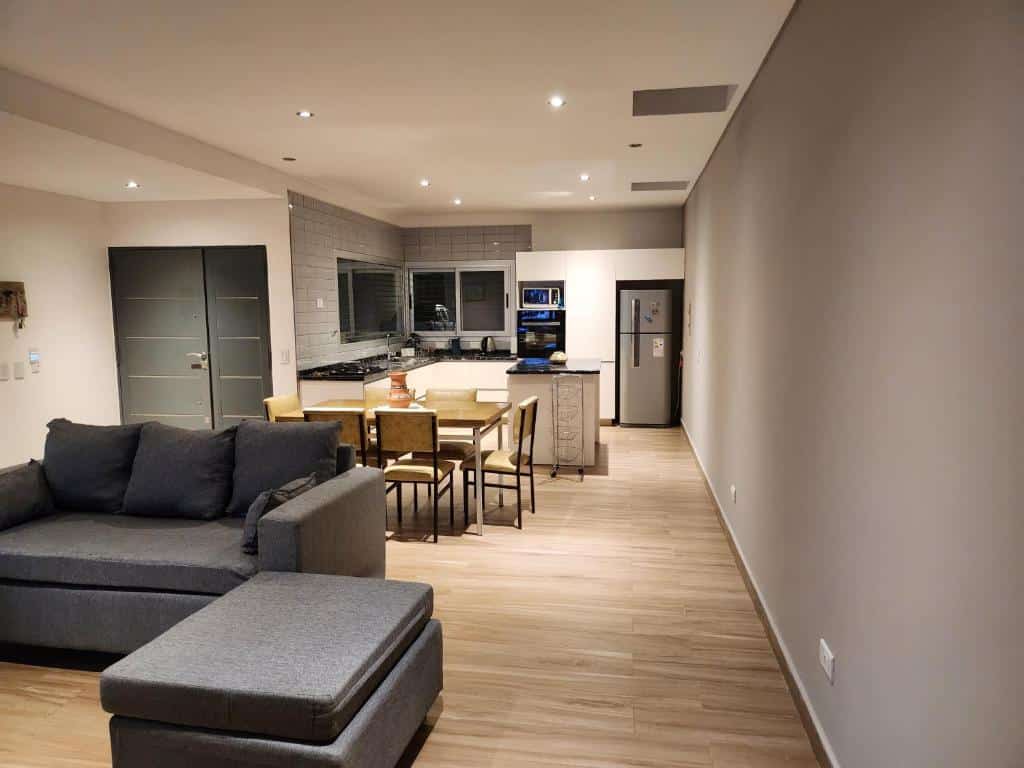 Moderna cozinha e sala de estar na Casa de Bruno em plano aberto com um sofá cinza, piso de madeira e paredes de cores neutras.