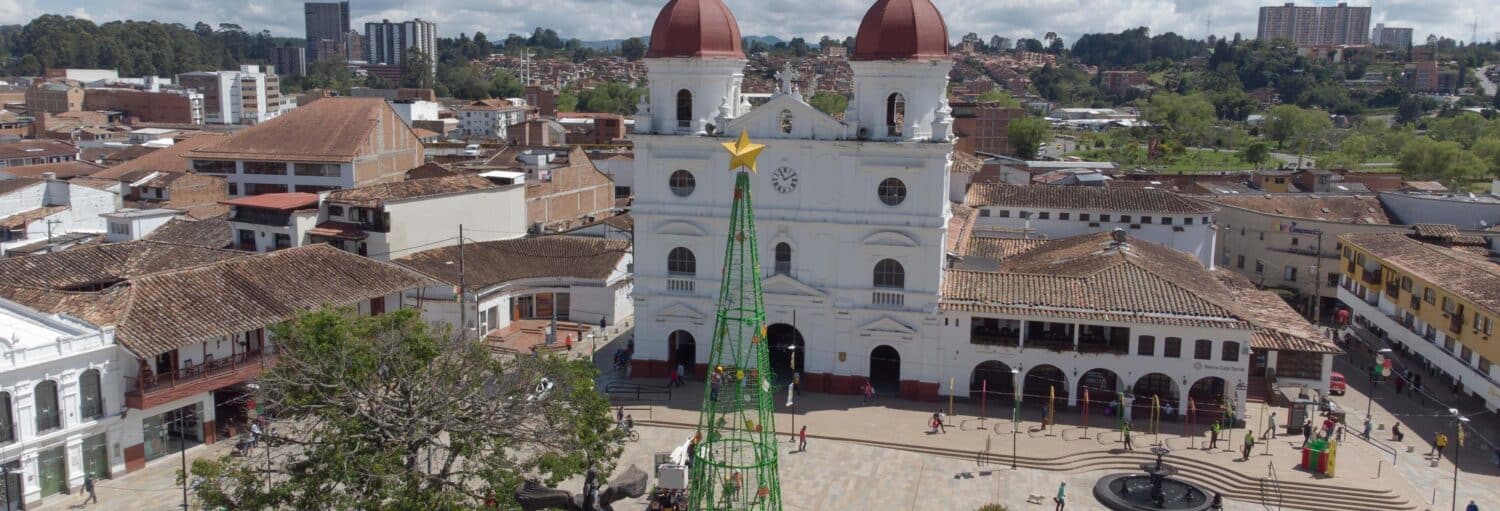 Vista aérea de uma praça da cidade com uma grande igreja, uma fonte e uma estrutura alta de arame para árvore de Natal. Imagem para ilustrar post sobre a excursão pelo leste de Antioquia.