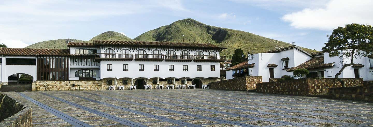 Uma grande praça de pedra com edifícios em estilo colonial e montanhas ao fundo sob um céu parcialmente nublado. a imagem ilustra o post sobre Excursão de Bogotá a Guatavita + Casa al Revés.