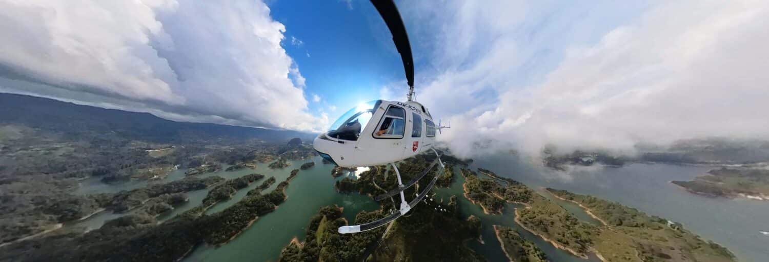 Um helicóptero branco sobrevoa uma paisagem de ilhas verdes e água azul sob um céu parcialmente nublado. Imagem para ilustrar post sobre a excursão privada de helicóptero saindo de Medellín.