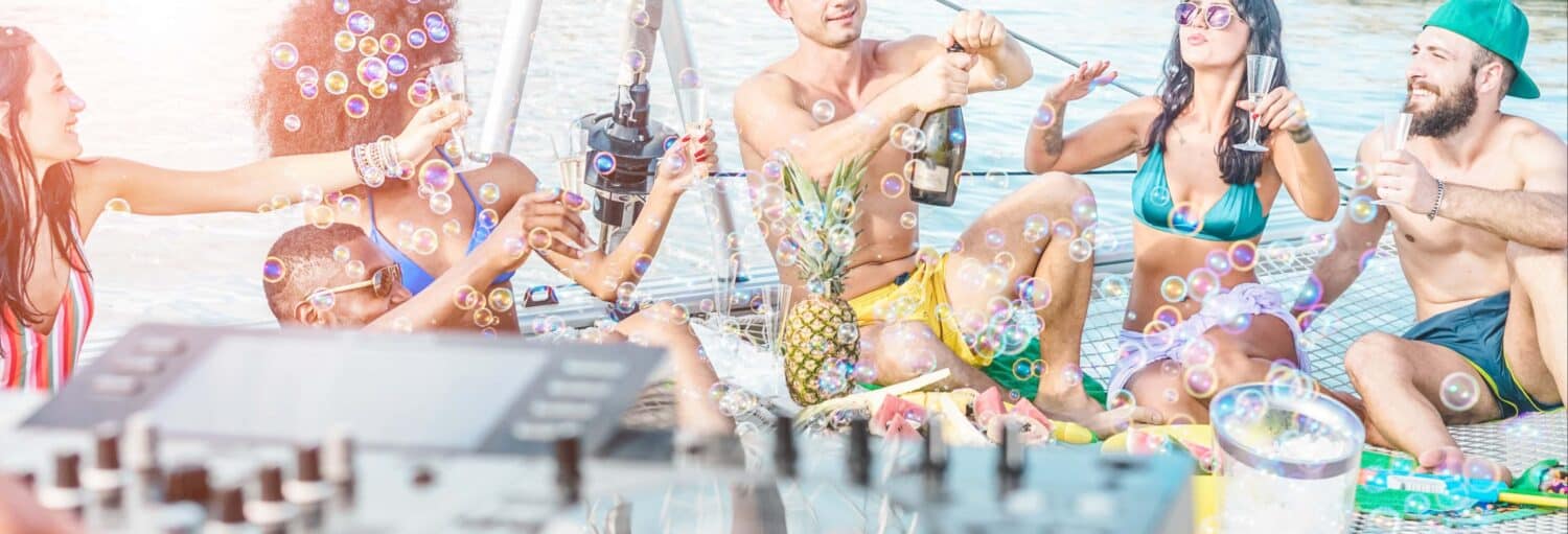 Grupo de jovens adultos em trajes de banho sentados em um barco, cercados por bolhas, com bebidas e um DJ à vista. Imagem para ilustrar post sobre festa de barco pela ilha Cholón.