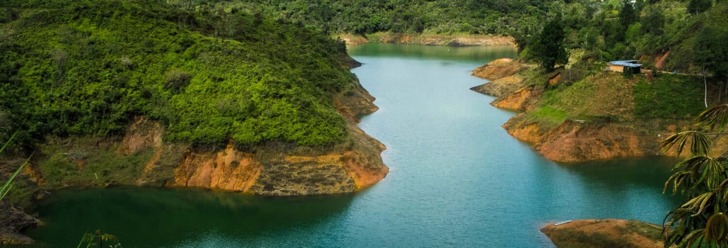 Um rio sinuoso com colinas verdes e uma pequena casa na margem direita, cercada por vegetação densa. Imagem para ilustrar post sobre jet ski ou wakeboard em Guatapé.