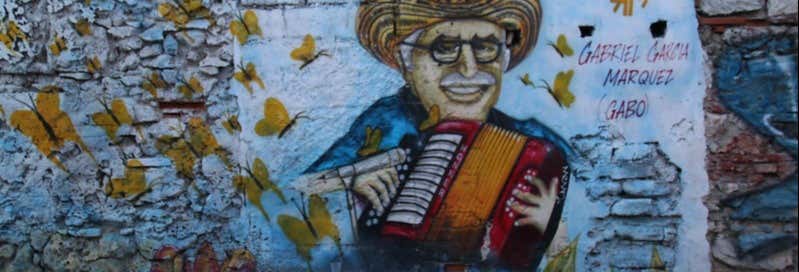 Um mural mostra um homem de óculos e chapéu tocando acordeão, cercado por borboletas amarelas e texto em uma parede desgastada pelo tempo. Imagem para ilustrar post sobre o free tour do Gabriel García Márquez.