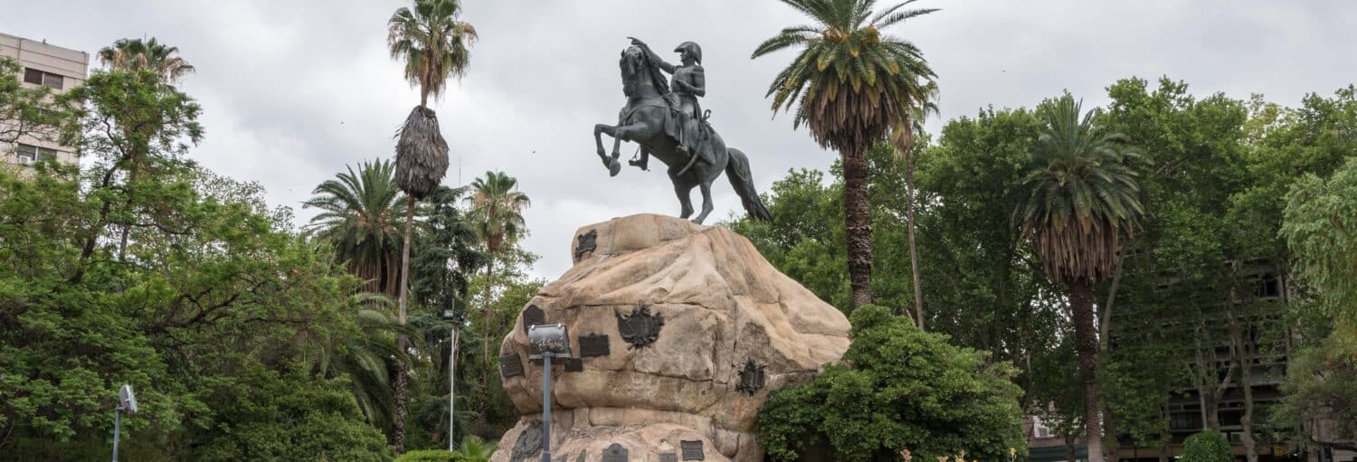 Estátua equestre em uma grande rocha cercada por palmeiras e vegetação sob um céu nublado durante o Free tour pela Cidade Nova de Mendoza