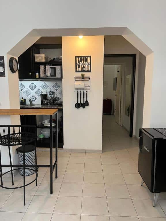 Cozinha pequena do Terrazas de Rondeau com armários pretos, utensílios de parede, backsplash estampado, uma mesa com banquetas e um corredor ao fundo.