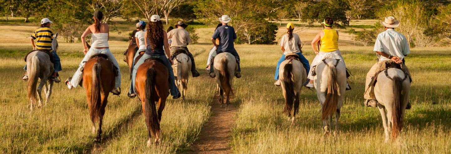 Oito pessoas desfrutam de um passeio a cavalo pelos Cerros de Guadalupe e Monserrate em uma trilha gramada, cercada por campos e árvores.