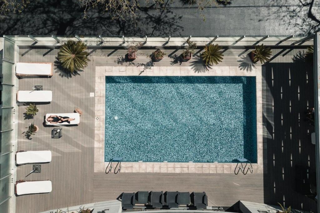 Vista aérea da piscina externa retangular do DiplomaticHotel com espreguiçadeiras ao redor e uma pessoa tomando banho de sol em uma cadeira. Imagem para ilustrar post sobre onde ficar em Mendoza.