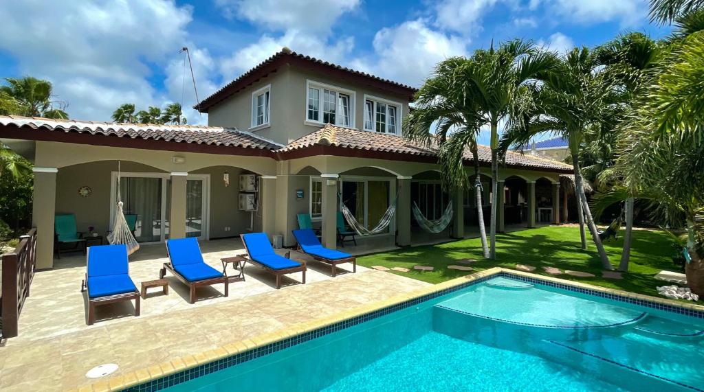 Quintal do Hibiscus Beach House com piscina, espreguiçadeiras azuis, redes, palmeiras e uma casa de dois andares sob um céu parcialmente nublado.