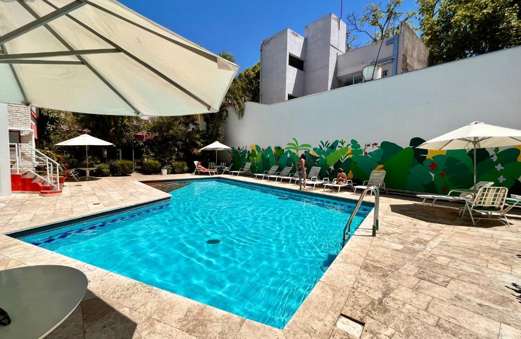 Piscina externa retangular do Hotel Nutibara com água azul clara, cercada por espreguiçadeiras, guarda-sóis e um mural em uma parede branca.