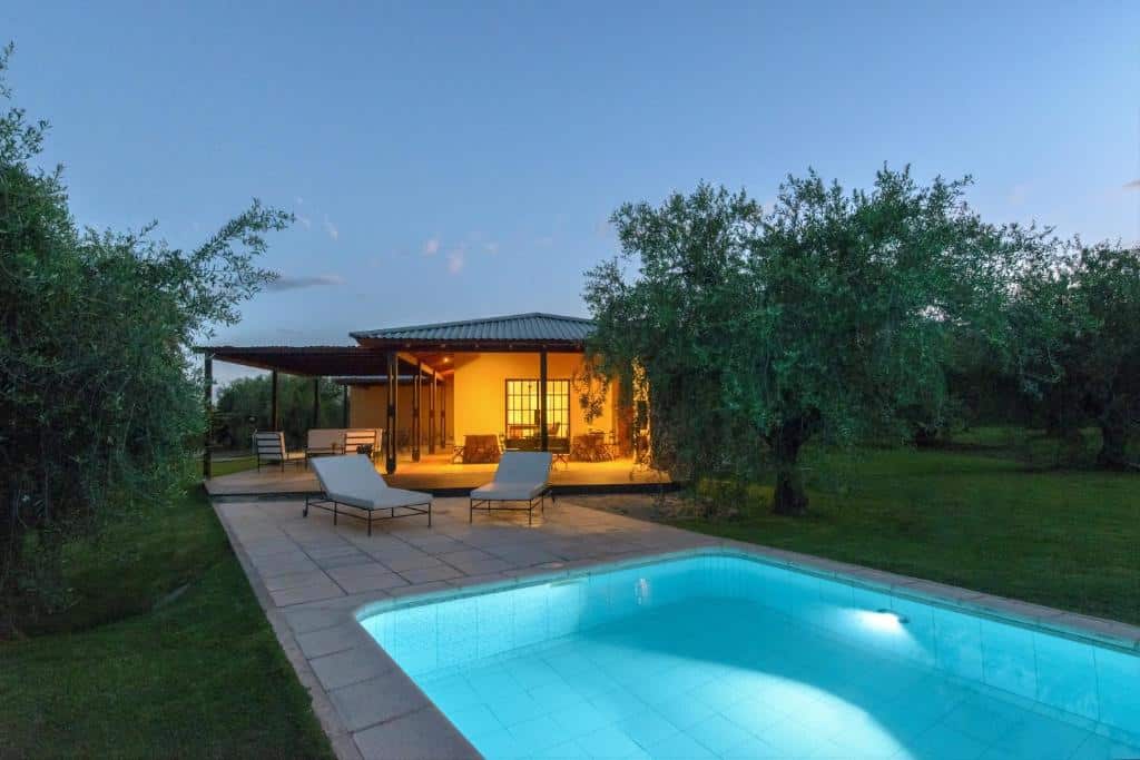 Posada Verde Oliva com um pátio iluminado, duas espreguiçadeiras e uma piscina, cercada por árvores ao anoitecer. Imagem para ilustrar post sobre onde ficar em Mendoza.