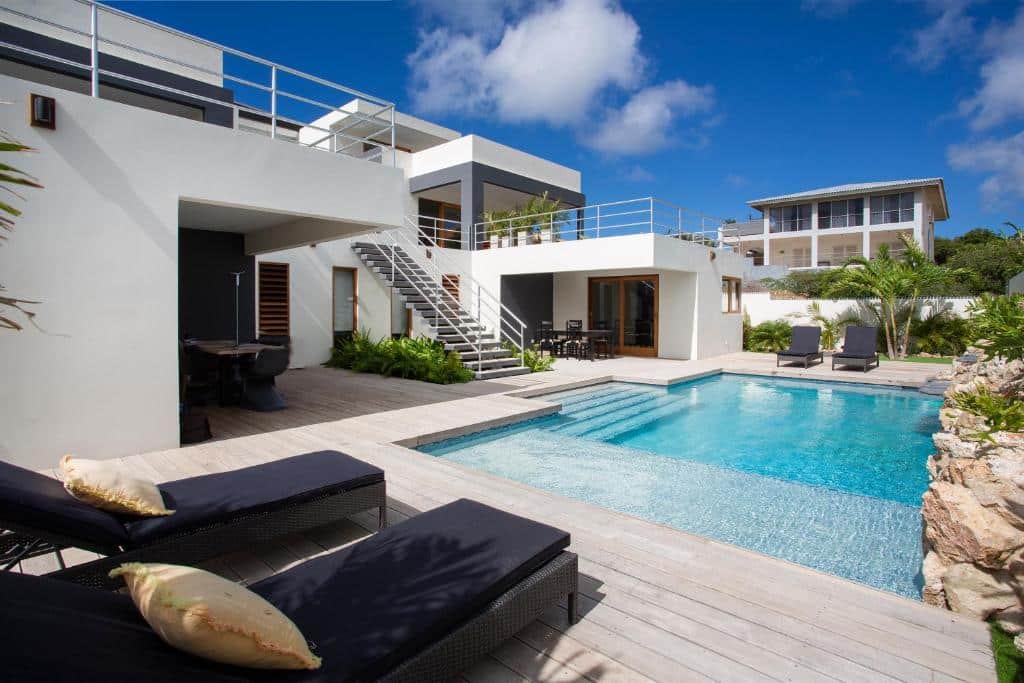 Villa Sol Paraiso com piscina privativa, espreguiçadeiras, área de pátio e escadas, situada sob um céu azul com nuvens dispersas.