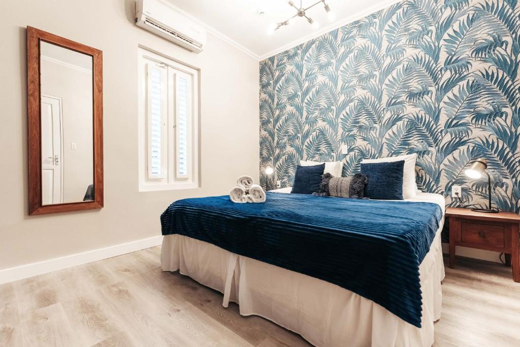 Um quarto do Atelier Skalo Boutique Hotel com uma parede de destaque com padrão azul, uma cama com roupa de cama azul, duas mesas de cabeceira e um espelho de parede.