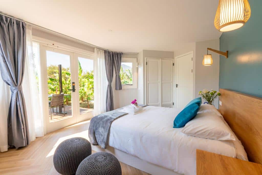 Quarto iluminado pelo sol do Bed & Bike Westpunt com cama de casal, parede com detalhes em azul, portas do pátio e assentos ao ar livre visíveis através de grandes janelas.