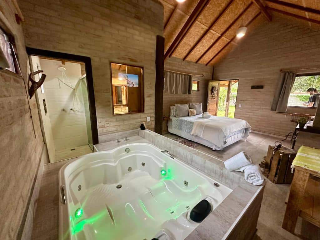 Quarto amplo no Chalé na Montanha, com uma cama de casal, uma banheira de hidromassagem para duas pessoas no canto esquerdo da acomodação, perto do banheio, toda a decoração é de madeira em estilo rústico