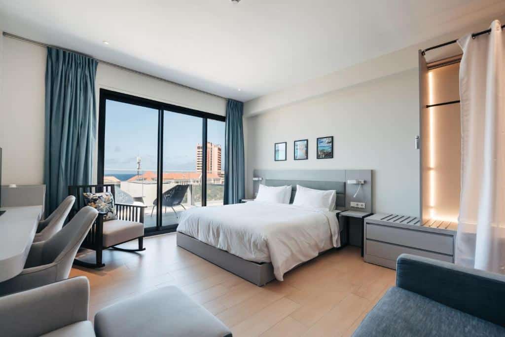 Quarto do Elements Hotel & Shops Curaçao com cama de casal, área de estar, varanda e janela grande com vista para a cidade e o mar.