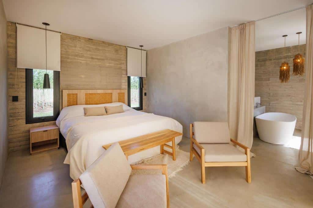 Quarto moderno do Lodge Tunuyan, Destino Uconia com uma cama de casal, móveis de madeira, tons neutros e uma banheira independente em um layout de plano aberto.