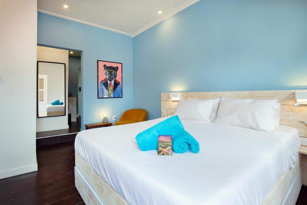 Uma cama bem arrumada do Wynwood Boutique Hotel com lençóis brancos, toalhas turquesa e uma pintura de um cachorro de terno em uma parede azul em um quarto moderno.