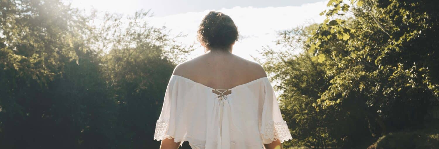 Uma pessoa com uma blusa branca está ao ar livre, de costas para a câmera, cercada por árvores e pela luz do sol. Imagem para ilustrar post sobre o tour de 2 dias pelo ecoparque Los Colores.