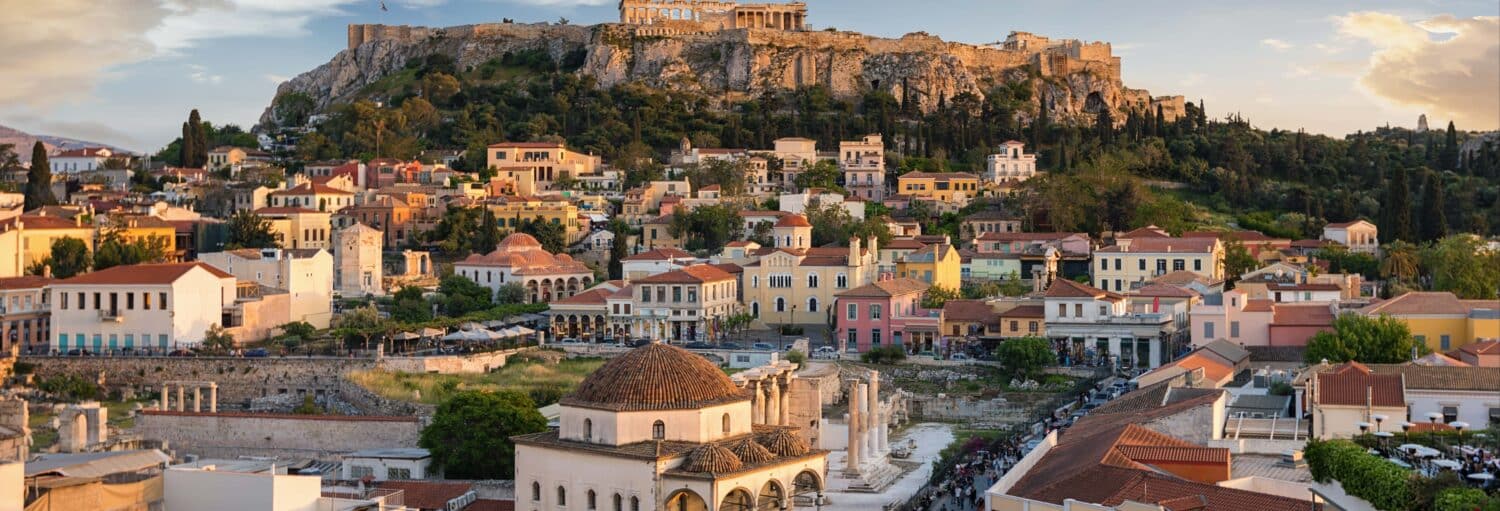 Vista de Atenas com edifícios coloridos em primeiro plano e a Acrópole em uma colina ao fundo. A imagem ilustra o post sobre Tour pela Atenas alternativa.
