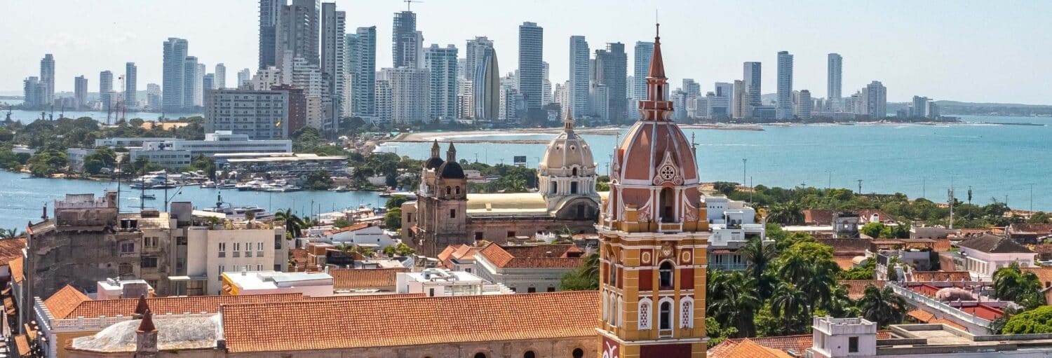 Uma paisagem urbana com edifícios coloniais em primeiro plano e arranha-céus modernos ao longo da costa ao fundo. Imagem para ilustrar post sobre o tour de chiva rumbera por Cartagena das Índias.
