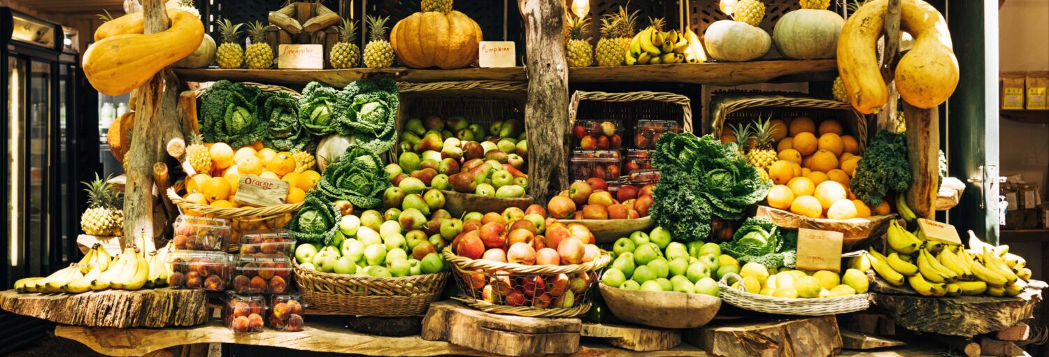 Frutas e legumes variados dispostos em cestas e prateleiras em uma exposição de mercado. Imagem para ilustrar post sobre o tour da fruta colombiana.