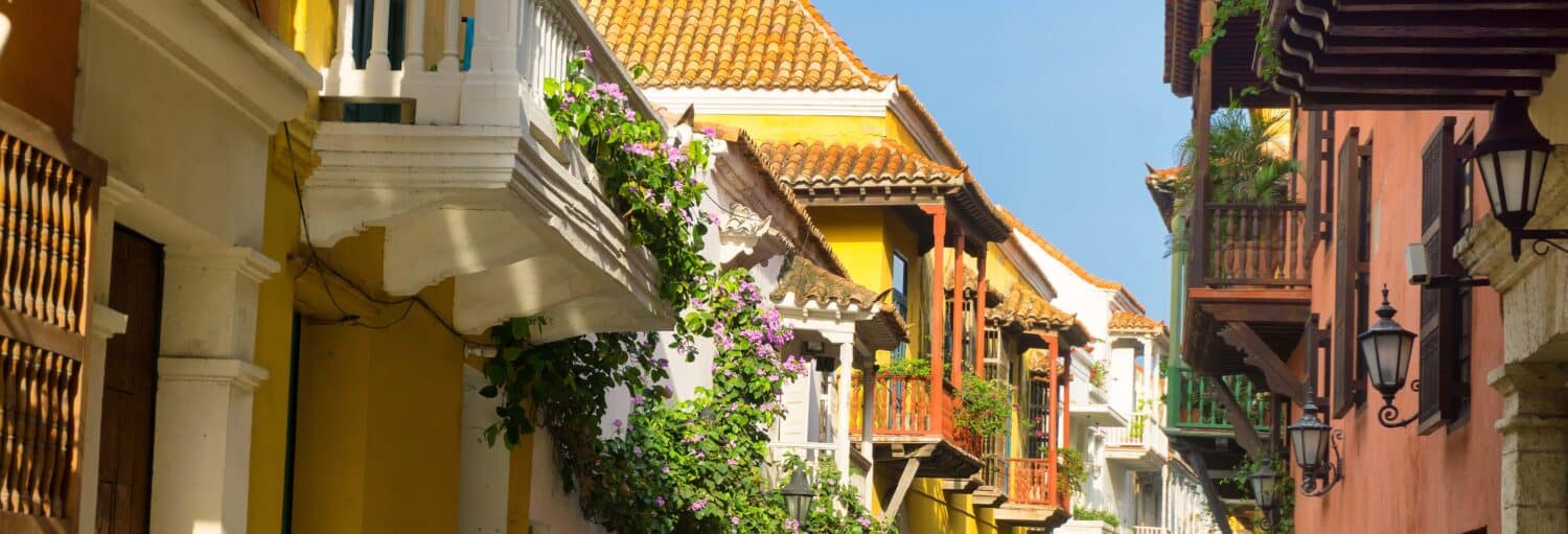 Prédios coloniais coloridos com telhados de telha e varandas com plantas verdes sob um céu azul claro. Imagem para ilustrar post sobre o tour das lendas de Cartagena.