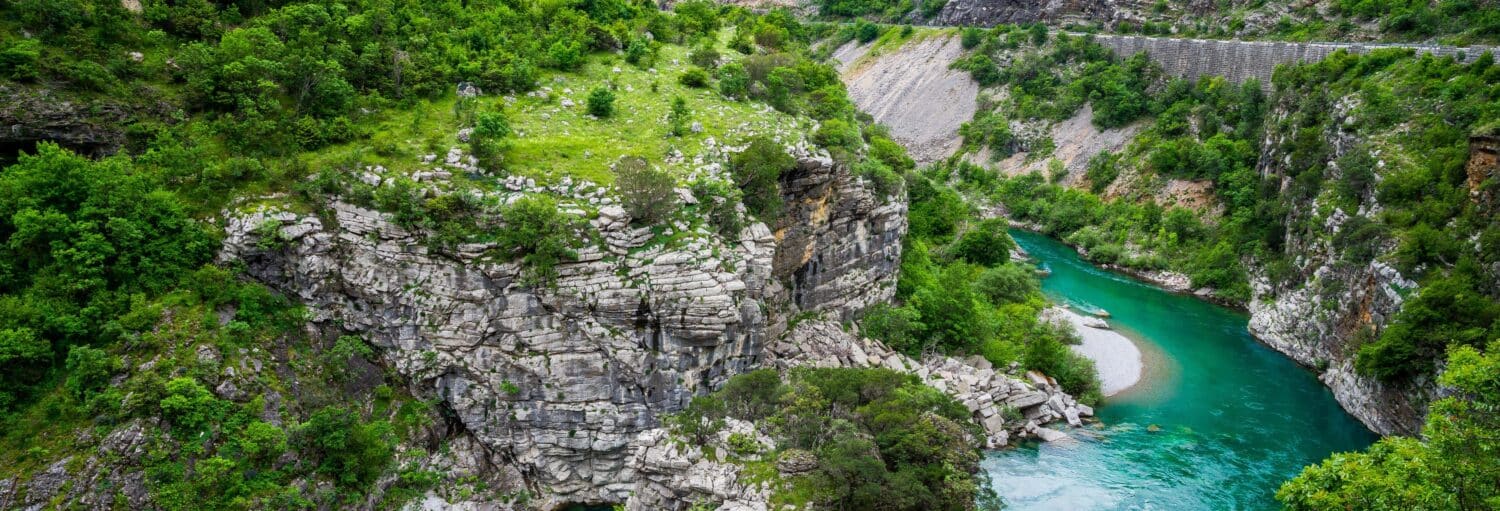 Um rio turquesa sinuoso flui ao lado de penhascos rochosos e vegetação verde em uma paisagem montanhosa, para representar Tour pela Planície de Zeta.