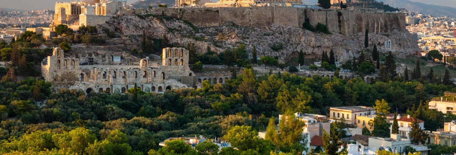 Vista da Acrópole e do Odeon de Herodes Atticus cercado por árvores e edifícios da cidade em Atenas, Grécia. A imagem ilustra o post sobre Tour de tuk tuk por Atenas.