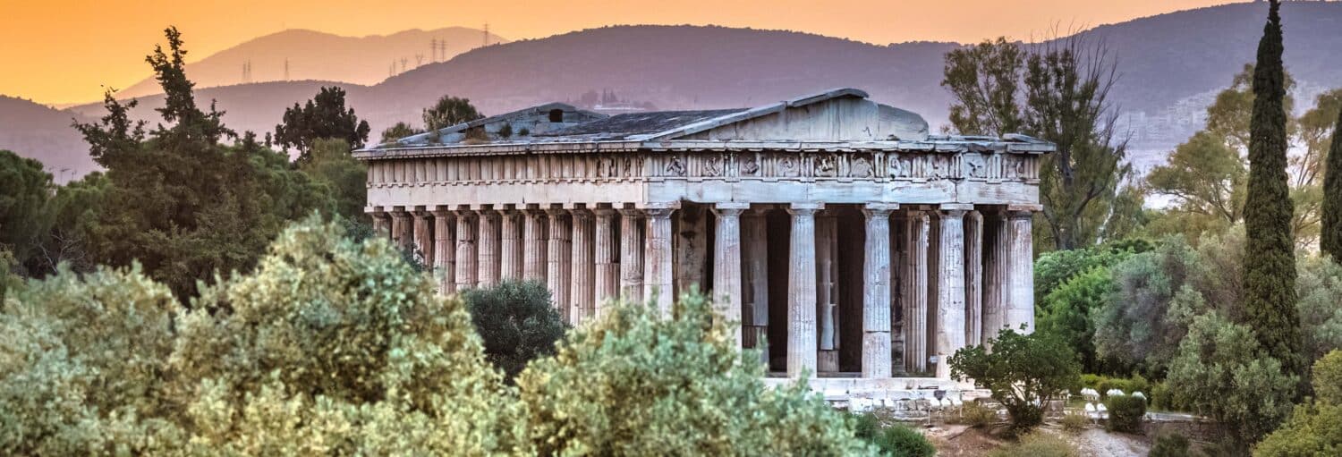 Templo grego antigo com colunas altas, cercado por árvores e colinas ao pôr do sol, ilustrando o post de Visita guiada pela Ágora de Atenas