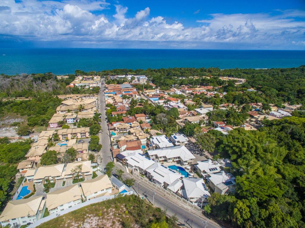 Vista aérea de uma cidade costeira com casas, estradas, árvores verdes e o oceano visível ao fundo sob um céu nublado.