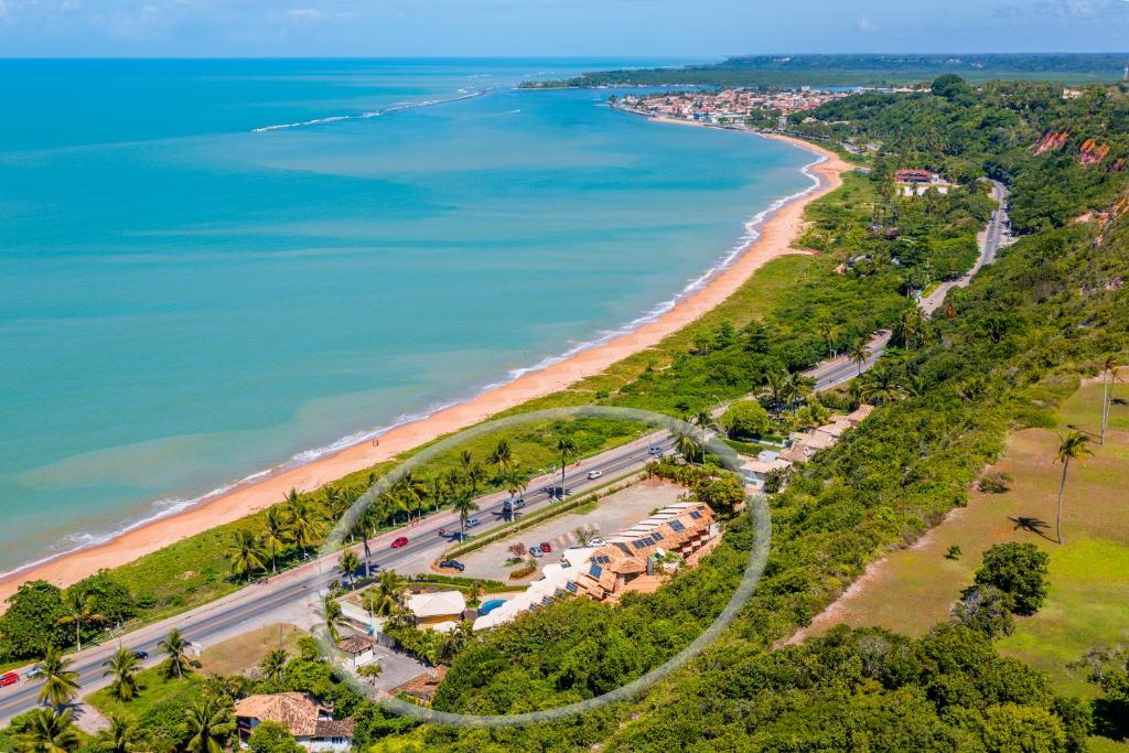 Vista aérea de uma estrada costeira ladeada por palmeiras, praia de areia e vários pequenos edifícios perto da costa.