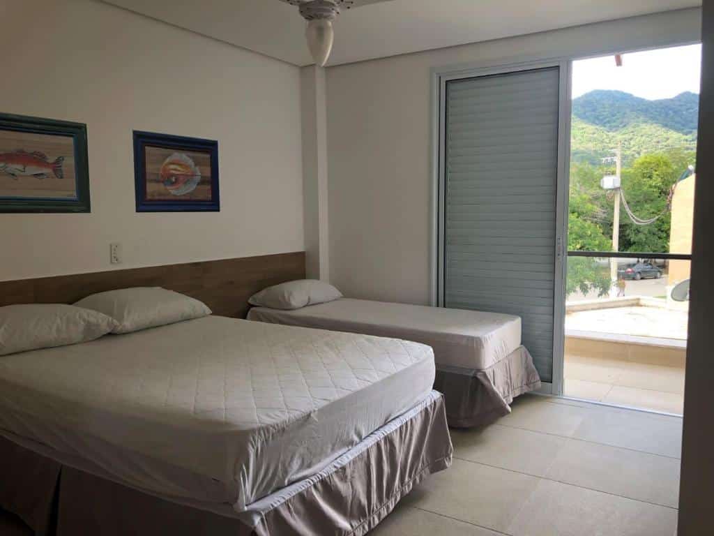 Um quarto da Casa na Praia Maravilhosa de JUQUEHY, um dos airbnb em Juquehy, com uma cama de casal e uma cama de solteiro, dois quadros, piso de azulejo e uma varanda com vista para as montanhas.