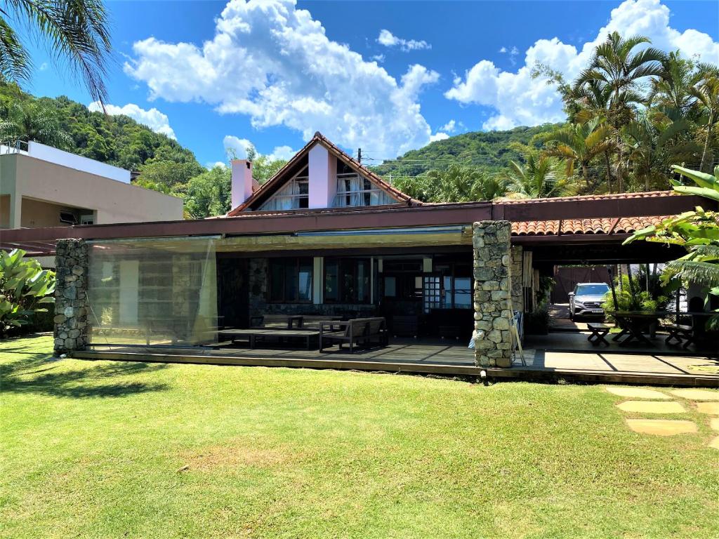 Uma casa de dois andares com um exterior de pedra e madeira, um pátio coberto e um gramado, cercada por árvores e colinas. Essa é a Casa pé na areia de revista.