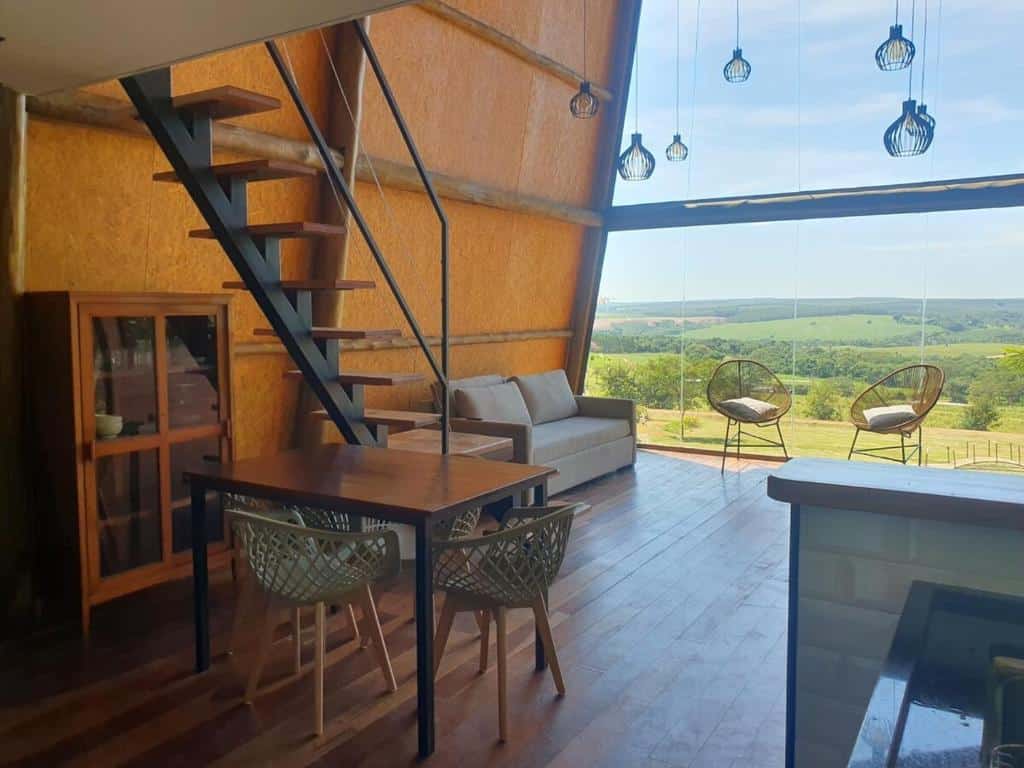 Uma sala de estar moderna com um loft, móveis de madeira, janelas grandes e uma vista panorâmica dos campos verdes e das colinas do lado de fora.