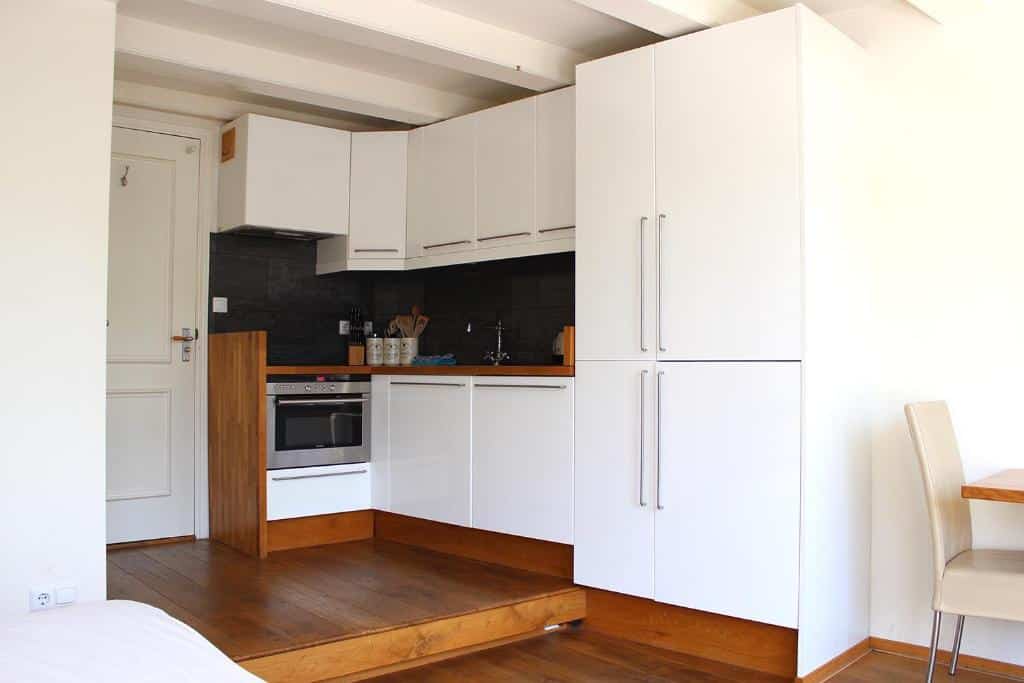 Foto do Amsterdam Jewel Canal Apartments. Cozinha moderna com armários brancos, forno embutido, backsplash preto e piso de madeira em um cômodo pequeno e iluminado.