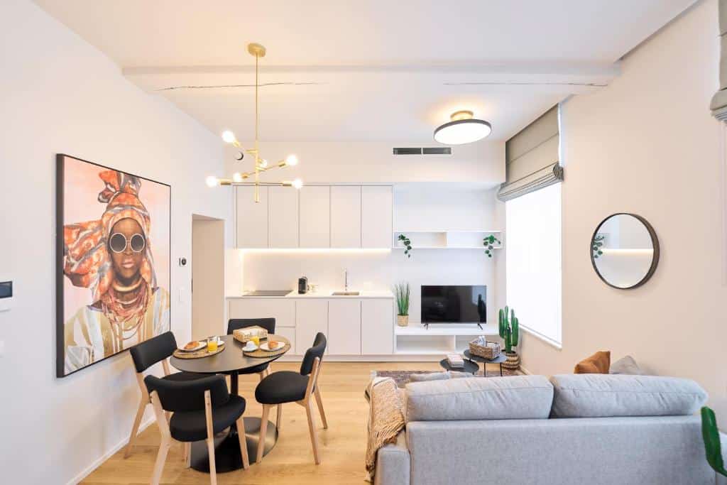 Moderna sala de estar e cozinha em plano aberto do Place du Grand com mesa de jantar, arte na parede, sofá, TV e uma grande janela que permite a entrada de luz natural.