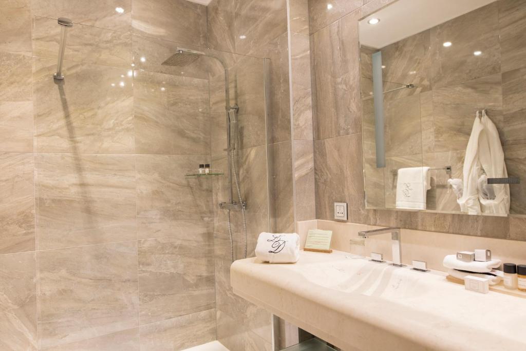 Banheiro moderno do Hotel Le Dixseptième com paredes de mármore bege, box de vidro, pia de bancada, espelho e produtos de higiene pessoal bem organizados. Imagem para ilustrar post sobre onde ficar em Bruxelas.