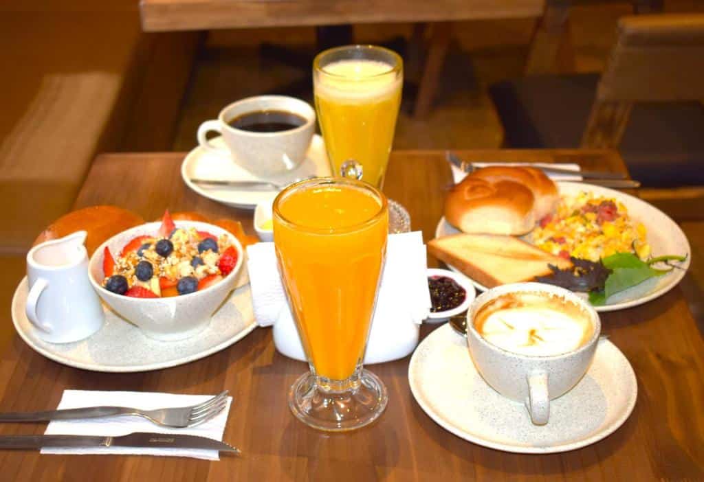 Um café da manhã da CASA MONTES PARDO com café, suco de laranja, tigelas de frutas, bolos, ovos mexidos, torradas e um cappuccino em uma mesa.