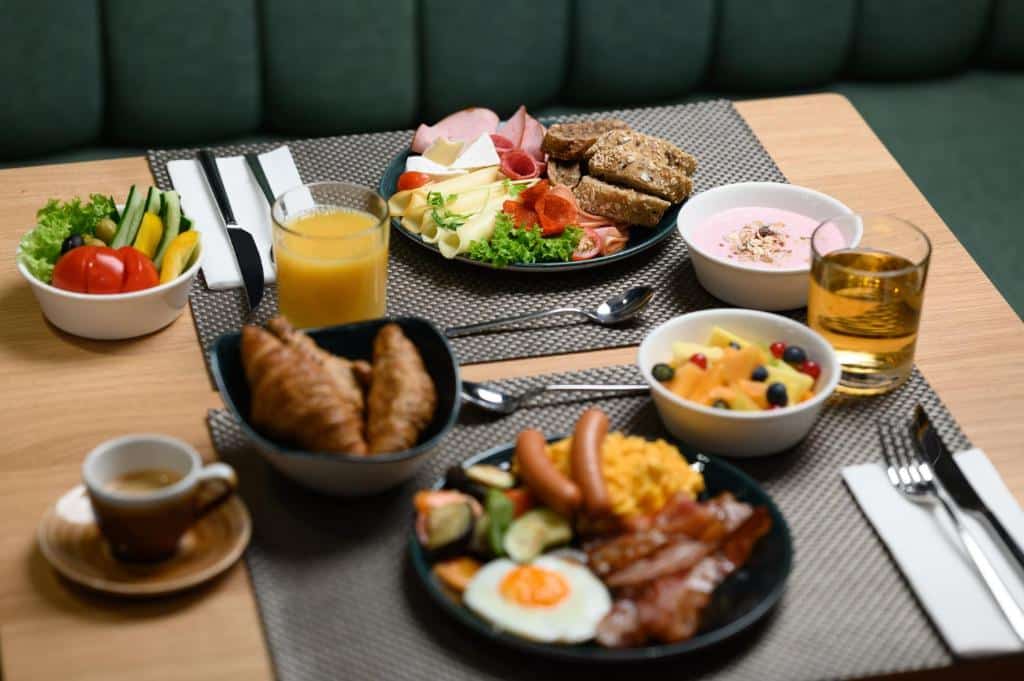 Uma mesa do Hotel Oktogon Haggenmacher posta para duas pessoas com um café da manhã que inclui croissants, ovos, frutas, frios, queijo, suco e café. Imagem para ilustrar post sobre onde ficar em Budapeste.