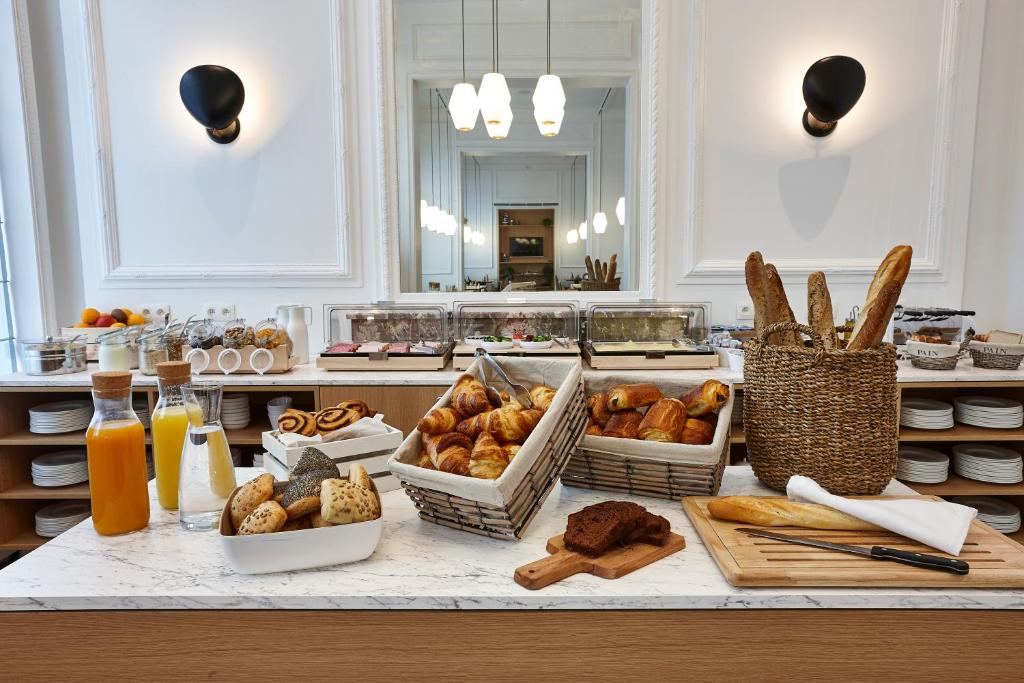 Um buffet de café da manhã do Hygge Hotel com bolos, pães, suco, frutas e talheres dispostos em um balcão de mármore em uma sala bem iluminada.