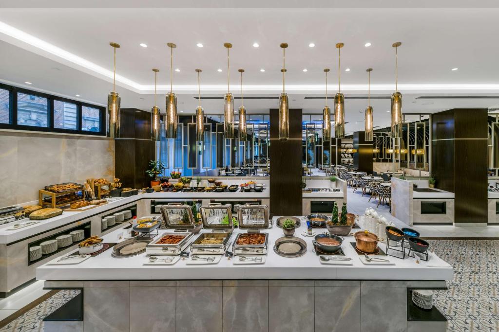 Um bufê do Radisson Blu Béke Hotel em uma sala de jantar moderna com vários pratos em bandejas e luzes pendentes penduradas acima. Imagem para ilustrar post sobre onde ficar em Budapeste.