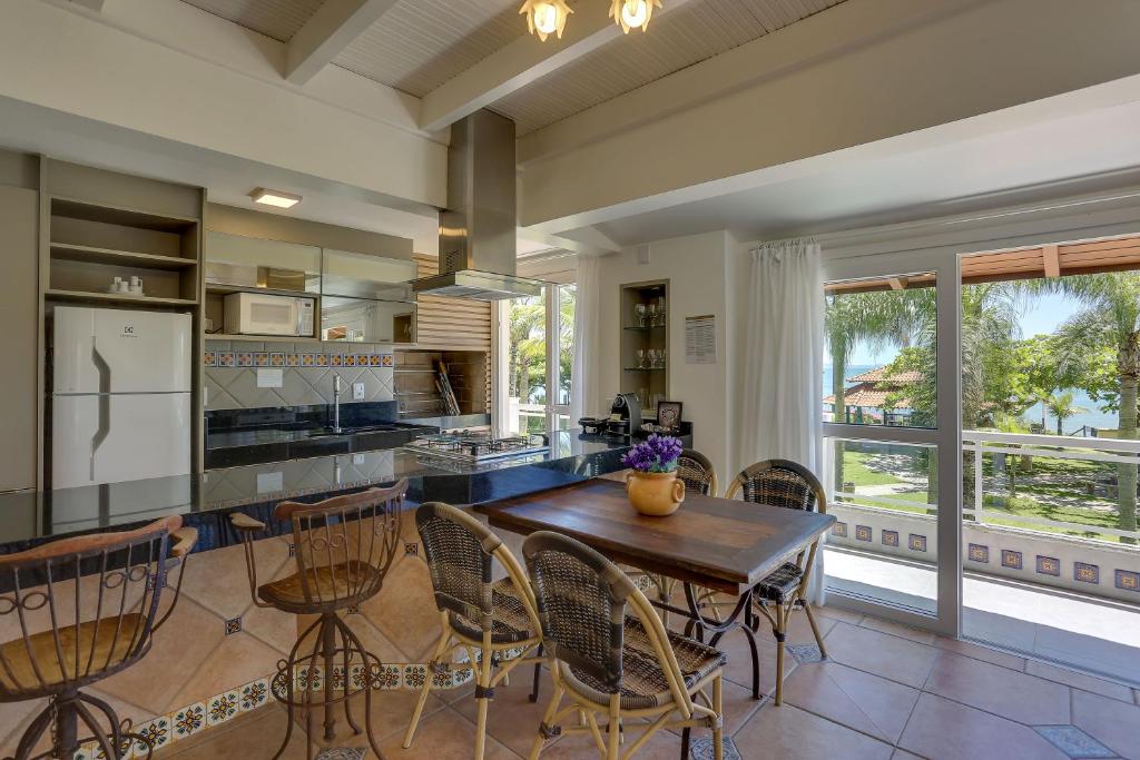 Cozinha espaçosa no Villas Jurerê Residences e área de jantar com assento em ilha, mesa de madeira e janelas grandes com vista para uma varanda e vegetação.