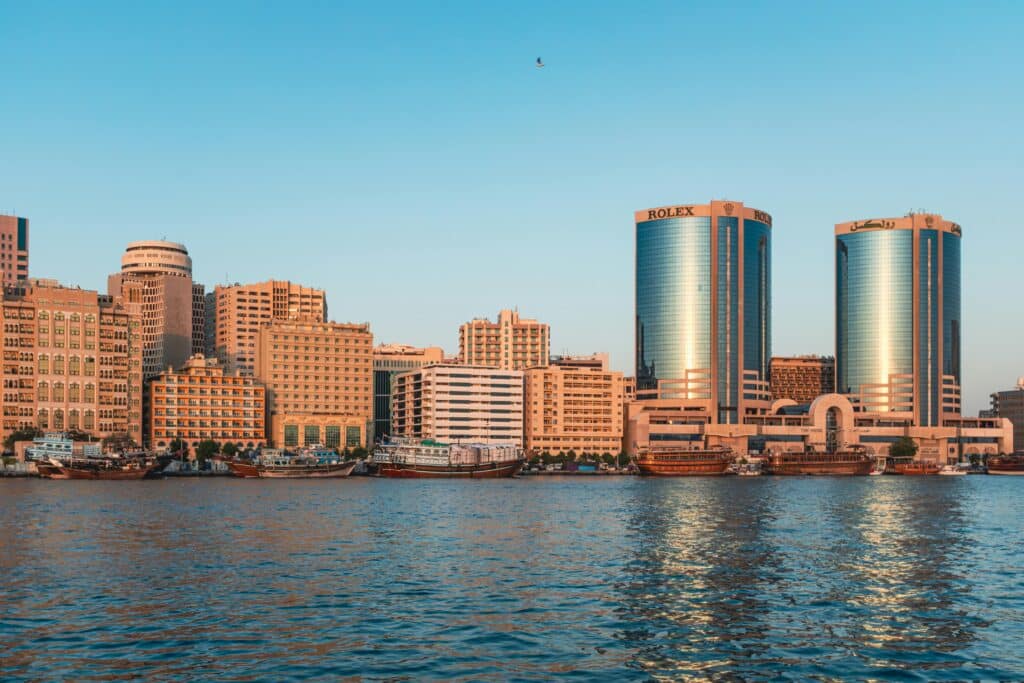 Horizonte da Deira, a partir do Creek, com prédios altos e barcos ao longo da orla, refletidos em águas calmas sob um céu azul claro.