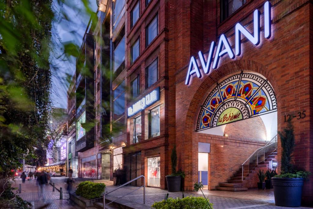 Vista da rua de um prédio de tijolos ao anoitecer, do hotel Avani Royal, com um grande letreiro AVANI acima de uma entrada em arco e luzes decorativas. Imagem para ilustrar post sobre onde ficar em Bogotá.