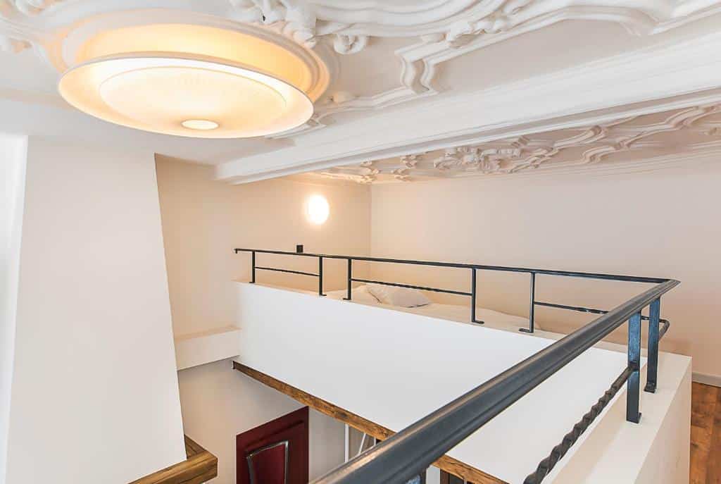 Um quarto loft do Hotel Agora Brussels Grand Place com uma grade preta, paredes brancas e um teto ornamentado com padrões intrincados e uma moderna luminária de teto.